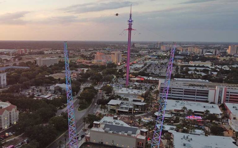 aerial view of riders on slingshot ride with lighted towers at sunset over international drive at orlando slingshot