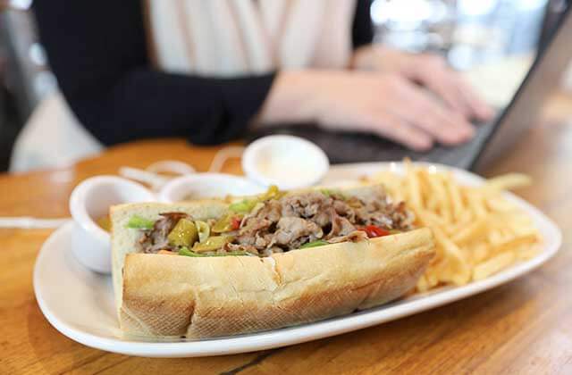 cheesesteak sandwich with sides on a tabletop with girl typing on laptop in the background at giordanos orlando kissimmee