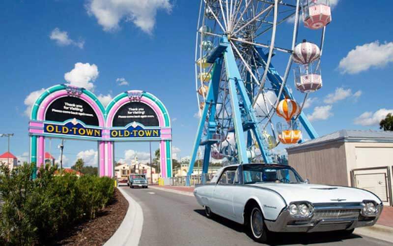 classic cars drive through a gateway and sign next to a ferris wheel at old town kissimmee