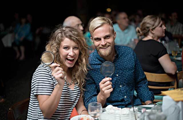 dining couple seated at a table with magnifying glasses at sleuths mystery dinner shows orlando