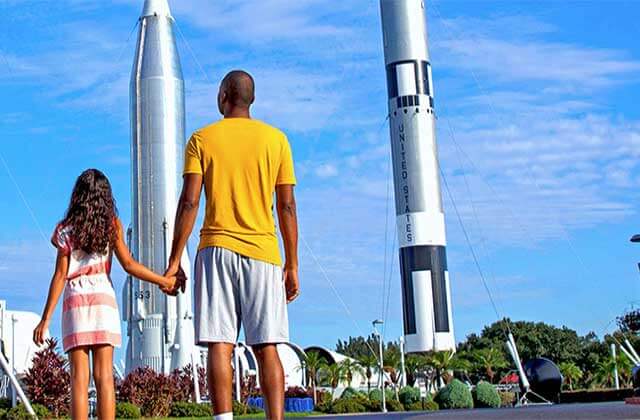 father and daughter stand facing two rockets kennedy space center visitor complex