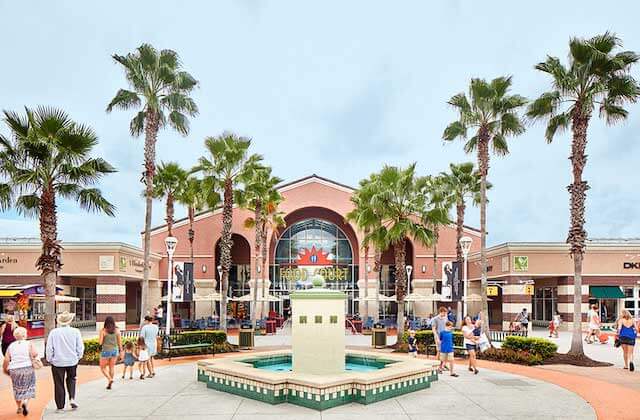 front exterior with fountain and plaza and food court entrance with shoppers and palm trees at orlando vineland premium outlets