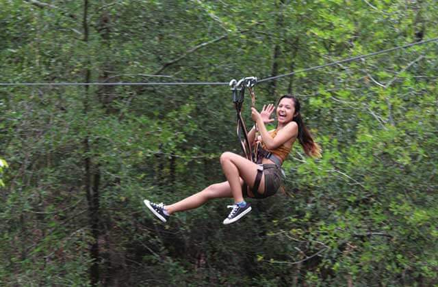 girl waves while passing on a zipline at orlando tree trek adventure park kissimmee