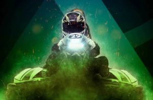 helmeted go karter driving with headlight with green lighting and dark background at andretti indoor karting games orlando