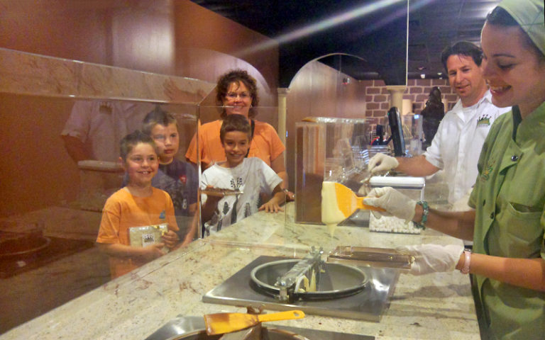 lady behind counter makes chocolate truffle with family watching at chocolate kingdom