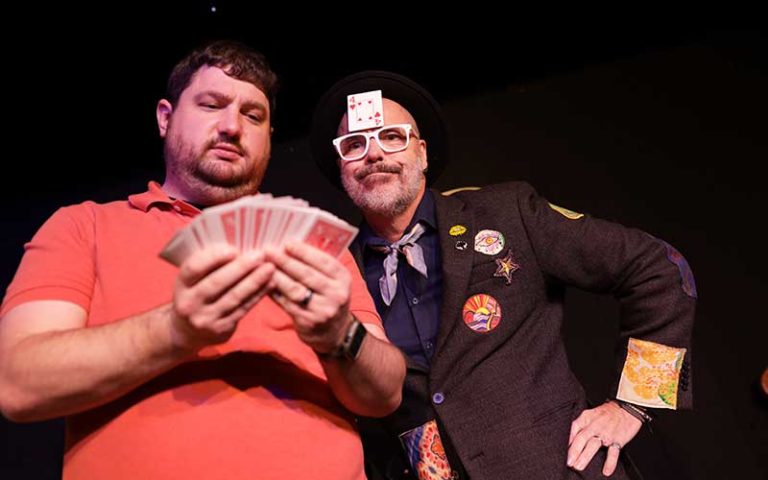 magician with playing card on forehead with volunteer picking through cards on stage at outta control magic comedy dinner show wonderworks orlando