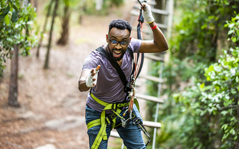 man excitedly moving along suspension bridge holding cable with forest background at orlando tree trek