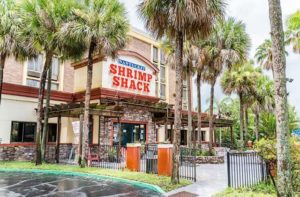 Exterior entrance of Nantucket Shrimp Shack in Kissimmee, Florida with stone work, red trim, pergolas, surrounded by tall palm trees and a fence