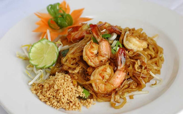 pad thai with shrimp rice lime garnish on white plate at thai thani