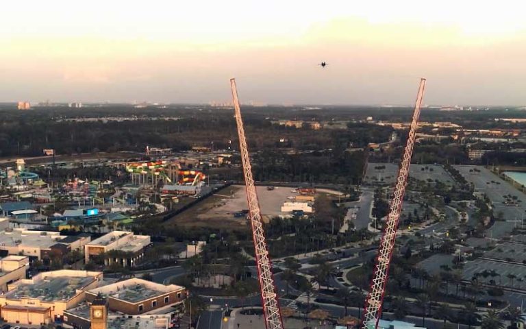 pair of towers with lights and ride suspended between with aerial theme park below at dusk at sunset walk promenade slingshot