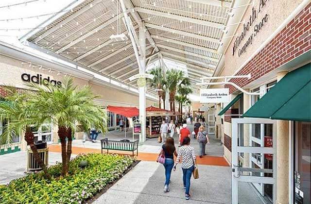 shoppers with bags walking in covered shopping area with adidas store orlando vineland premium outlets