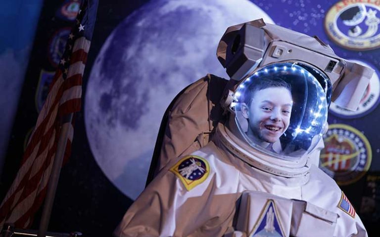smiling boy in nasa space suit with moon and space behind at wonderworks orlando
