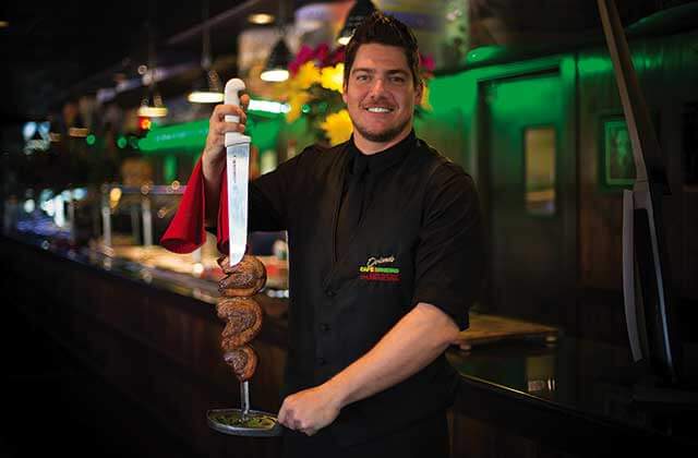 smiling chef holds skewer with filets mignon at cafe mineiro brazilian steakhouse orlando