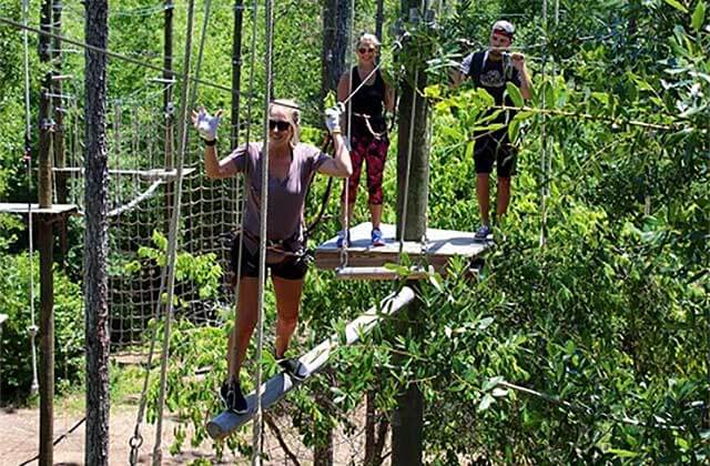 smiling woman crosses log bridge orlando tree trek adventure park kissimmee