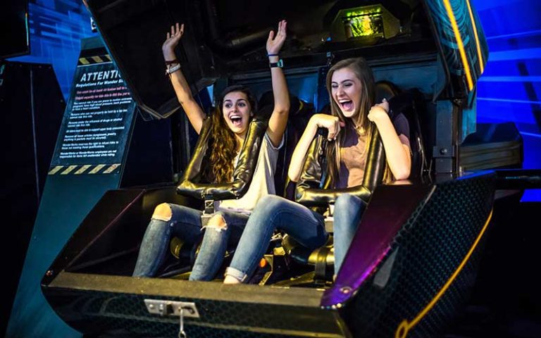 teen girls laughing and screaming seated in roller coaster 3d simulator at wonderworks orlando