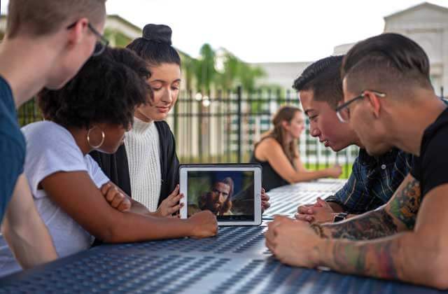 teens gather outside at table watching film on tablet at jesus film project orlando