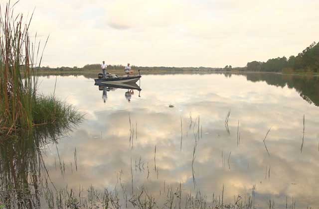 two men fishing on a boat on a placid lake with reflected sky at revolution adventures clermont