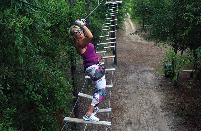 woman smiles while scaling an inclined rope ladder at orlando tree trek adventure park kissimmee