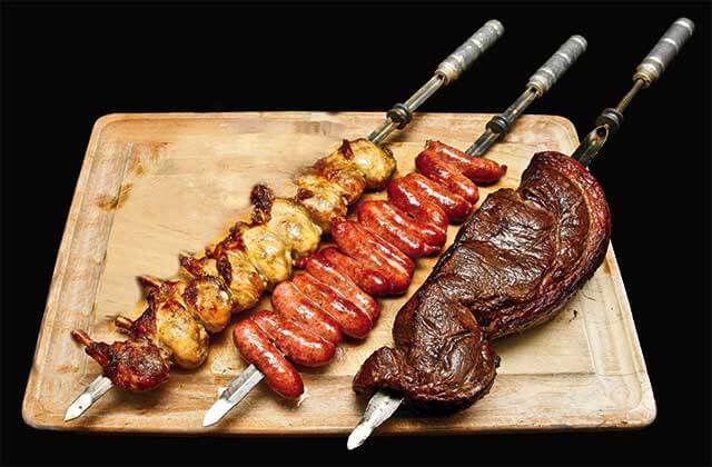 wooden cutting board with skewers of chicken sausage and steak at cafe mineiro brazilian steakhouse orlando