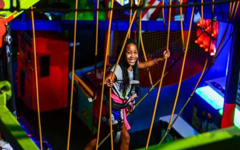 young girl climbing along rope course with neon colors at wonderworks orlando