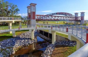 stately pedestrian skywalk bridge with kissimmee trail sign with spiraling ramp over road and rocky creek with trees and scenery destination feature