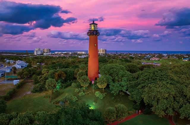 aerial view of red lighthouse with surrounding trees with purple cloudy twilight sky at jupiter inlet lighthouse museum florida