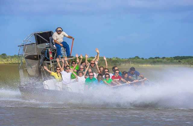 airboat with waving riders speeds across wetlands at everglades alligator farm florida city