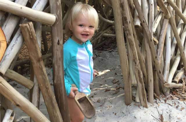 child peaks out from bamboo forest while playing in the sand at palm beach zoo florida