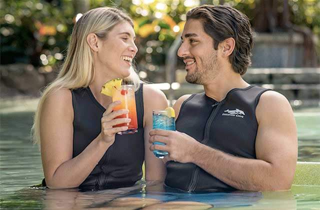 couple in wetsuits in a pool talking with cocktails at discovery cove orlando