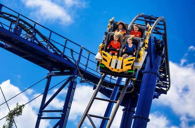 four kids with mouths open on a yellow coaster speeding down blue rails at legoland florida resort