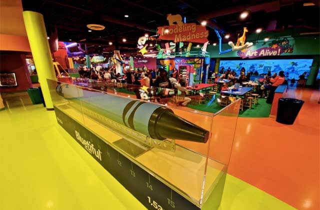 giant blue crayon in a display case with an art classroom area at crayola experience orlando