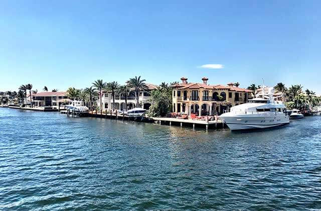 luxury boat moving through inlet with homes and docks at delray yacht cruises