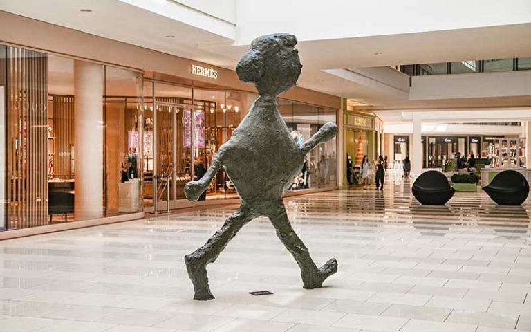 metal sculpture of walking figure inside atria at aventura mall miami