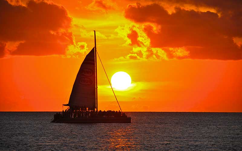 orange sunset over water with a large crowded catamaran at fury water adventures key west