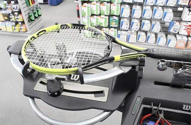 racquet being restrung on a machine in equipment repair area of store at tennis plaza florida stores