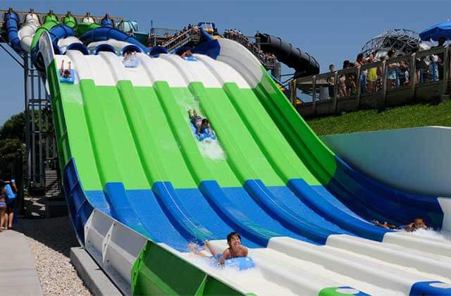 row of green blue and white slides with riders on mats at rapids water park west palm beach