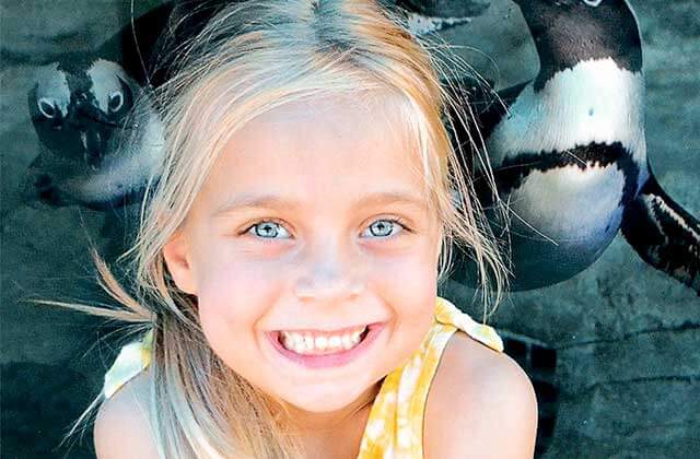 smiling blue eyed blonde girl posing in front of penguins in a habitat at miami seaquarium florida