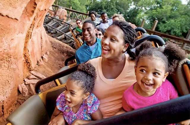 smiling family riding a roller coaster at disney magic kingdom theme park orlando