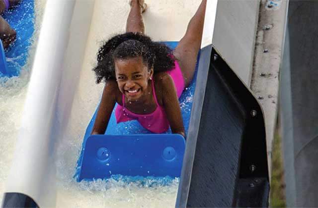 smiling girl on a mat sliding down a chute at big kahunas water adventure park destin
