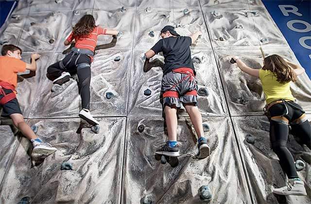 teens scaling a rock wall wearing harnesses at off the wall gamezone coconut creek florida