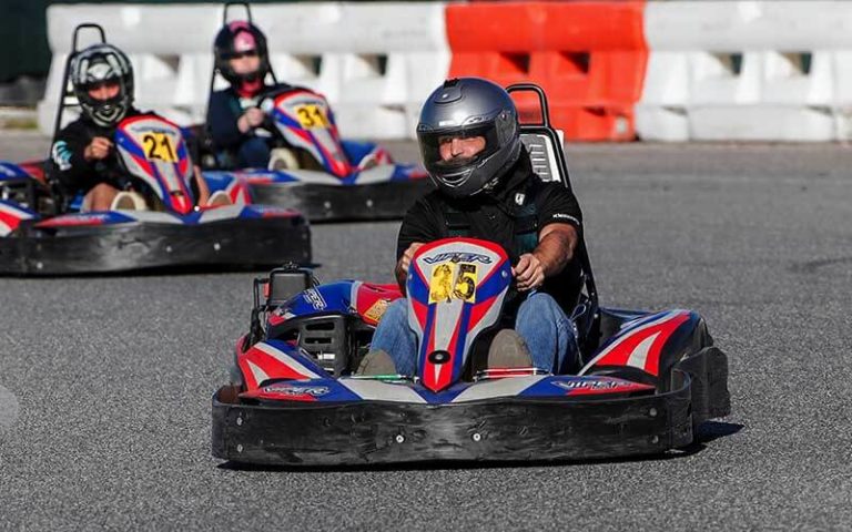 three kart racers in helmets racing around bend on track at orlando kart center
