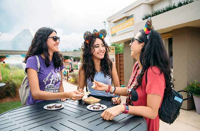 three young ladies share food festival samples over a table at disney epcot theme park orlando