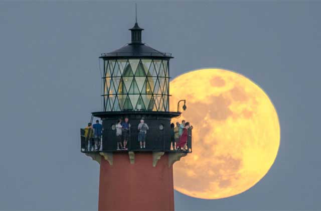 top of lighthouse with people on balcony and huge orange moon in the background at jupiter inlet lighthouse museum florida