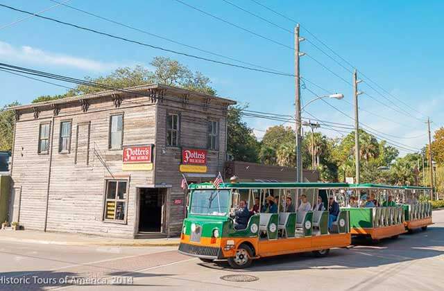 trolley bus passing a wooden building with potters museum sign at old town trolley tours st augustine