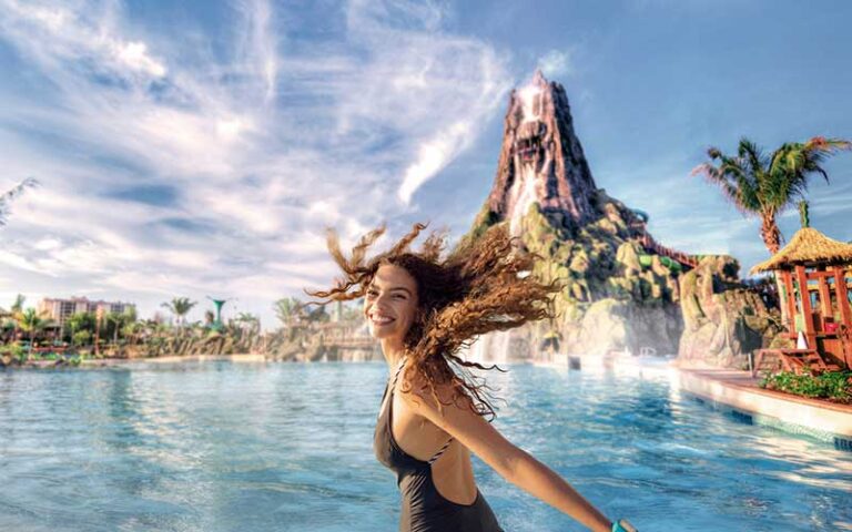 young lady flipping her hair in wave pool with volcano slide background at universal volcano bay orlando
