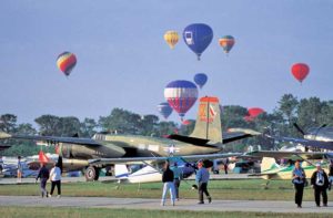 airfield with vintage aircraft on grass with tree line and colorful hot air balloons in the sky at lakeland destination feature