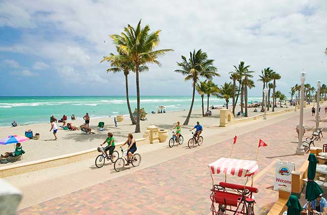 brick boardwalk along beach with pedicab bikers palm trees beachgoers at hollywood florida destination feature