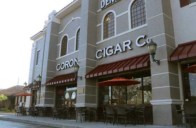 front exterior of tan building with red awnings and outdoor seating at corona cigar company orlando