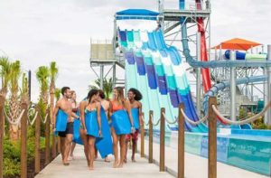 laughing teens carrying slide mats with slide towers in the background at island h2o live waterpark kissimmee