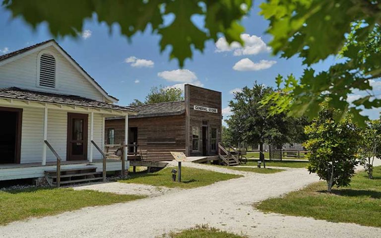 reconstructed pioneer buildings with gravel roads and trees at pioneer village
